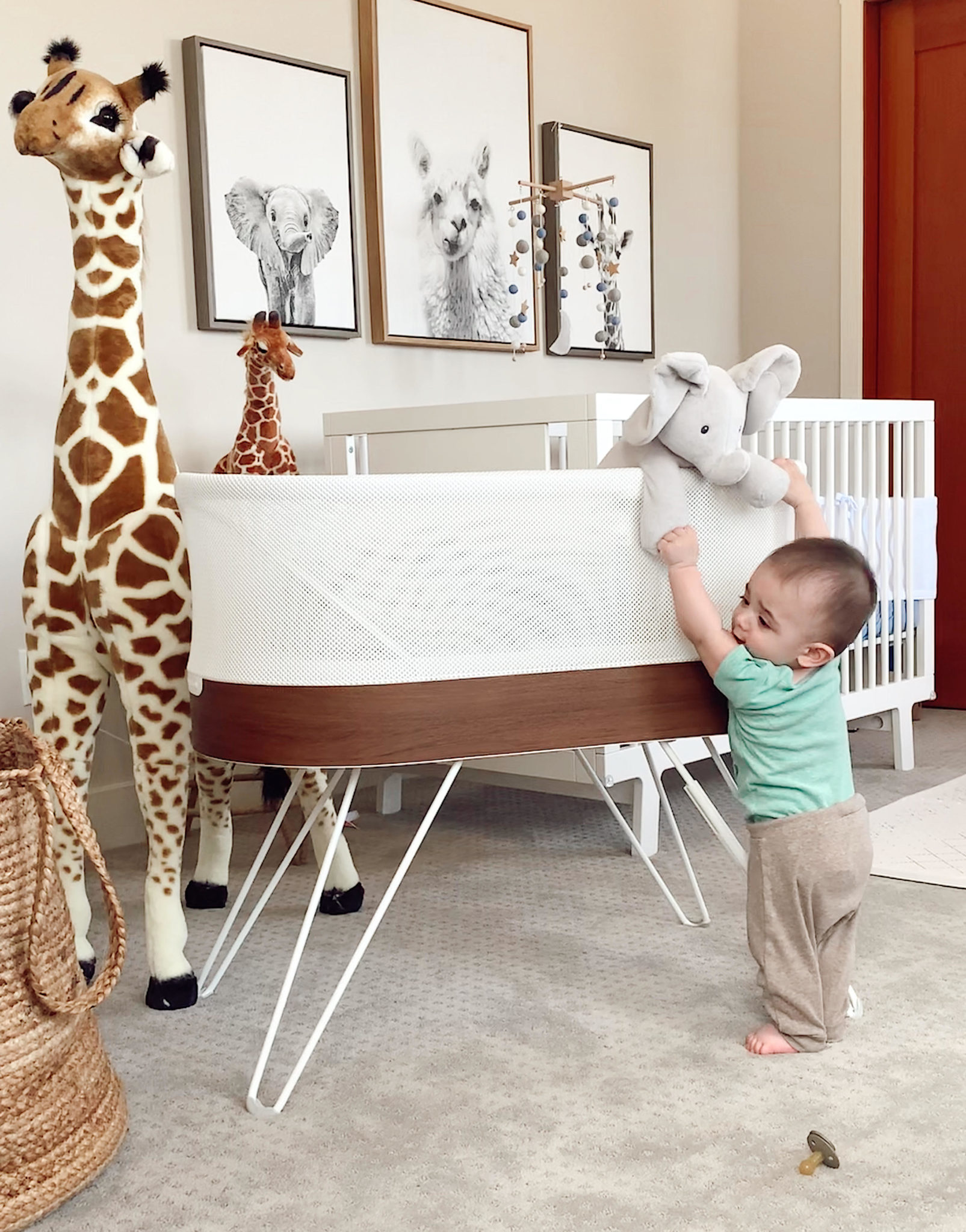 newborn baby products I actually used | Newborn Baby Items by popular San Francisco motherhood blog, Just Add Glam: image of a baby boy standing next to a bassinet and a life size stuffed giraffe.