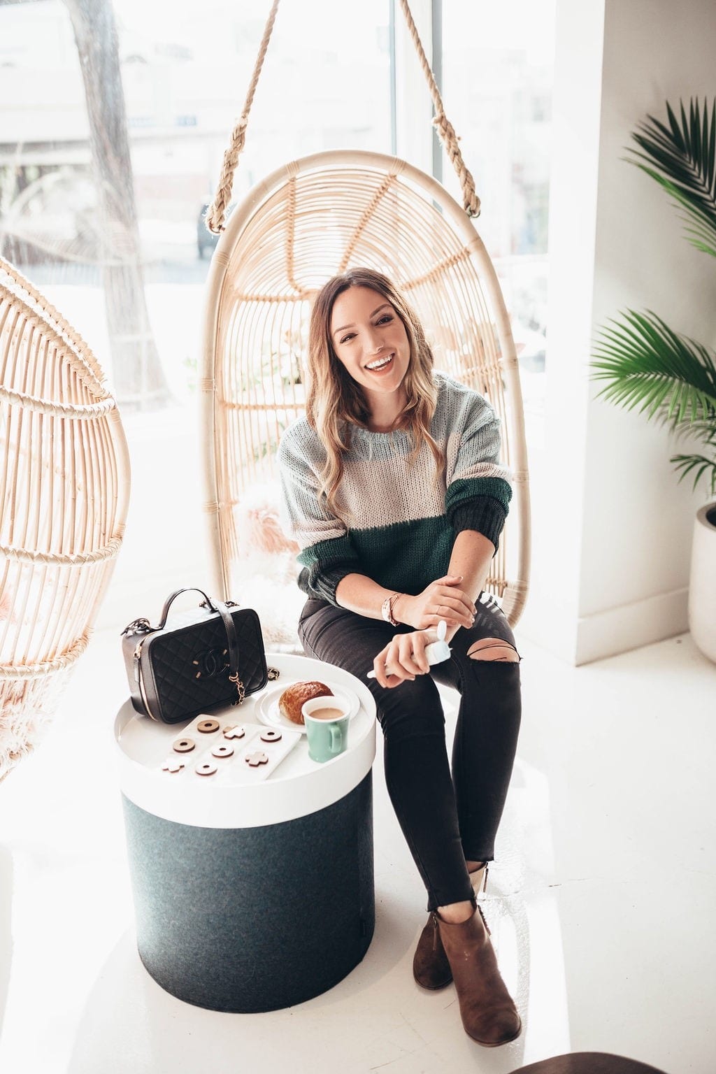 How to Heal Dry Hands by popular San Francisco lifestyle blog, Just Add Glam: image of a woman sitting in a hanging rattan chair and applying lotion to her hands. 
